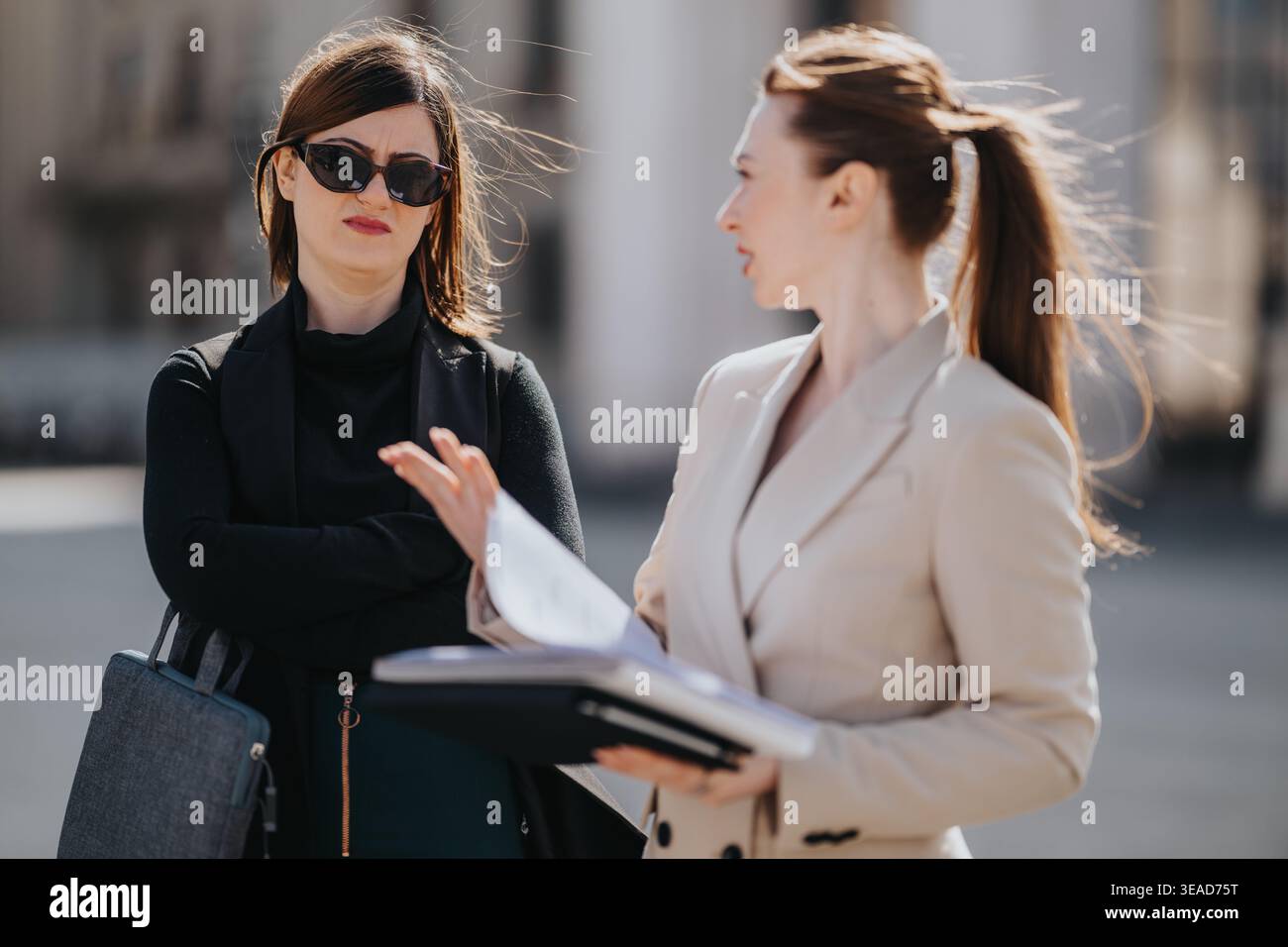 Businesswomen having a tense discussion outdoors over documents, colleague looking frustrated Stock Photo