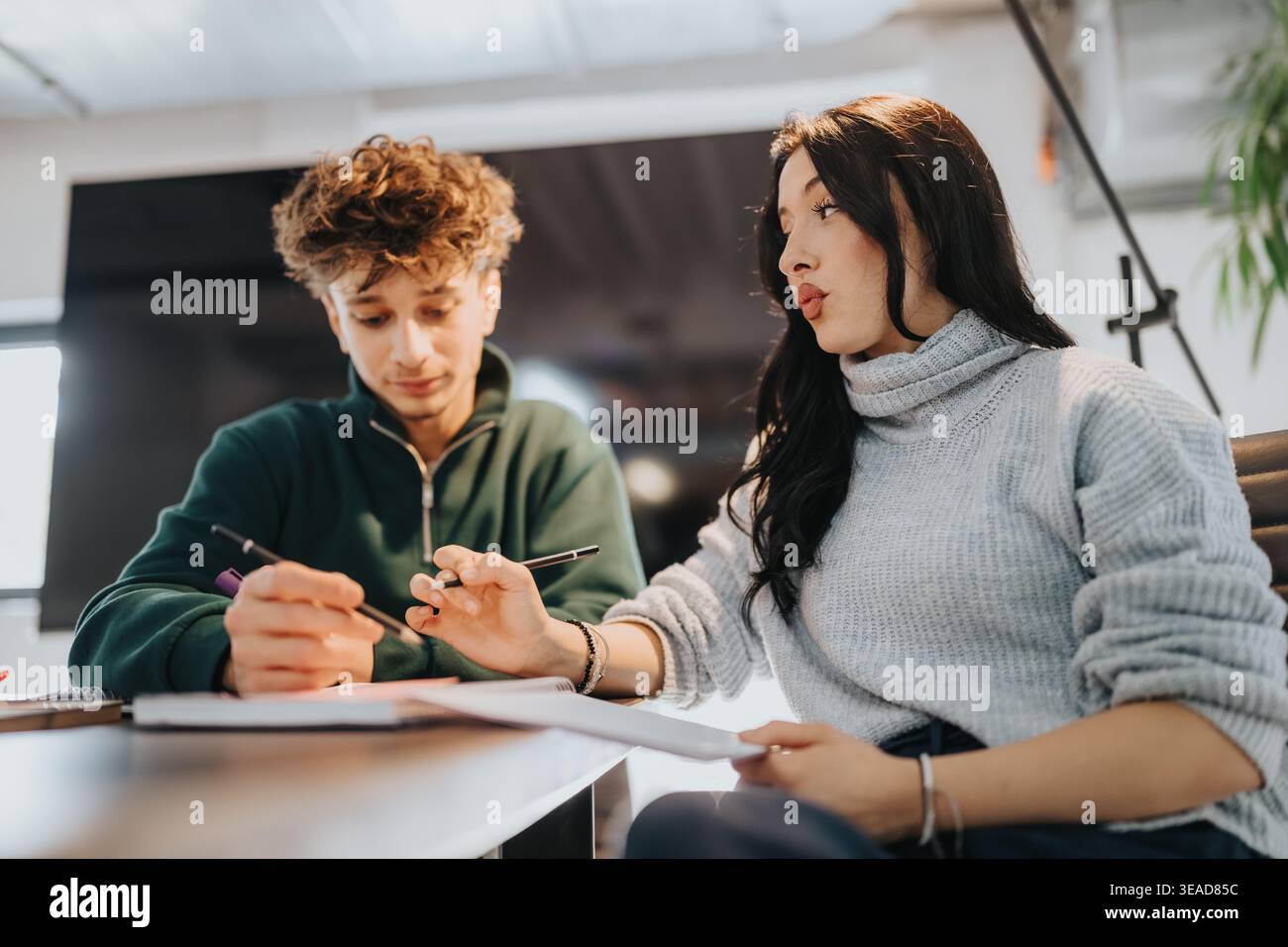 Two students collaborating on homework and studying together at a modern classroom table Stock Photo