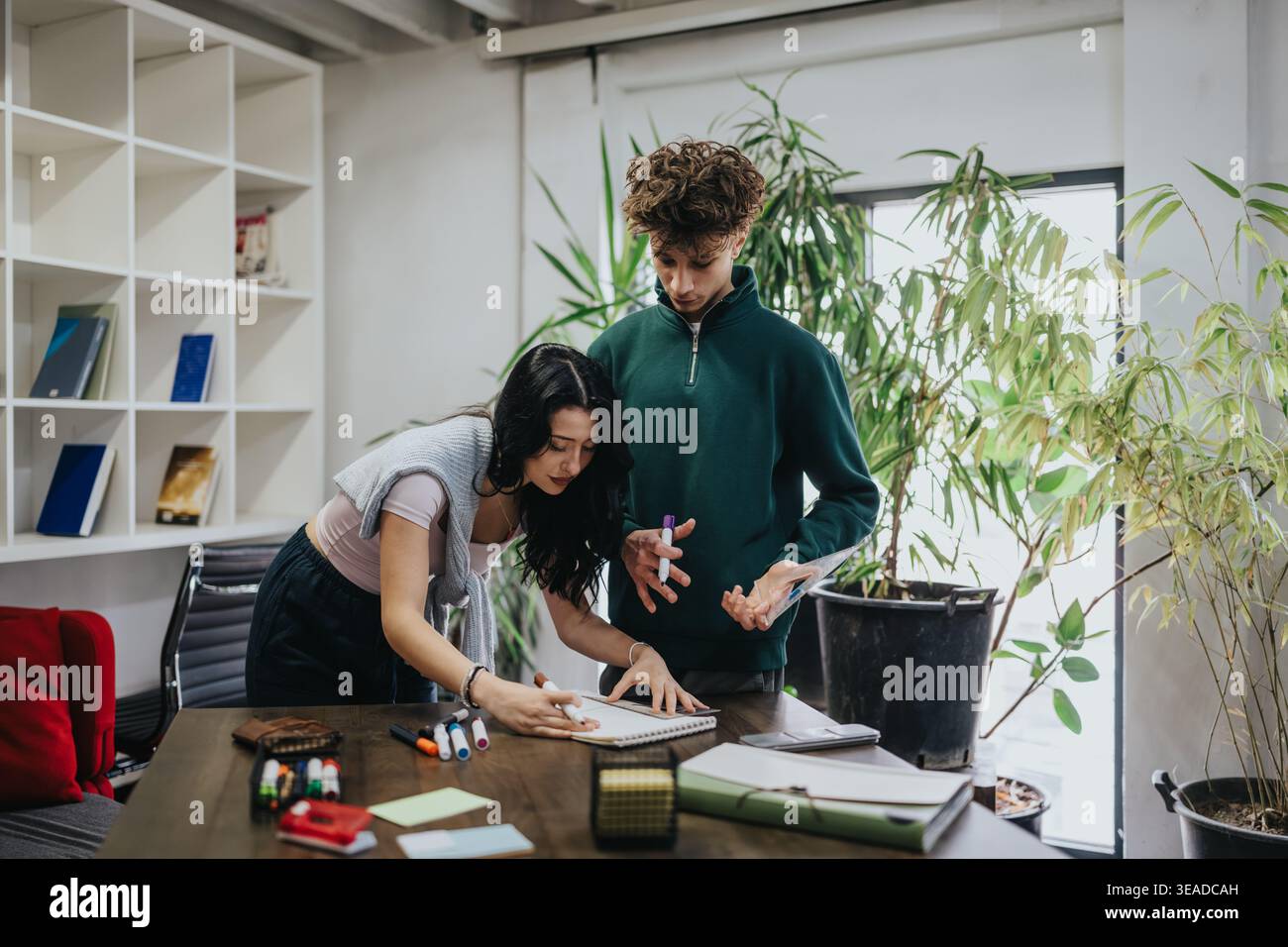 Two students collaborating on a project at a table in a modern study workspace Stock Photo
