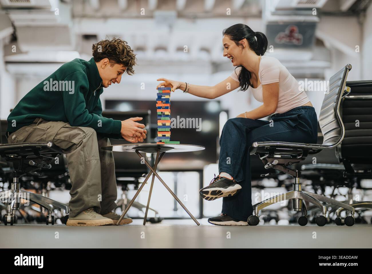 Two students playing a tabletop block game together in a modern co‑working or study space Stock Photo