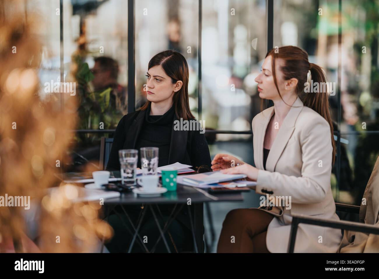 Business meeting between two professional women discussing documents and coffee at an outdoor cafe table Stock Photo
