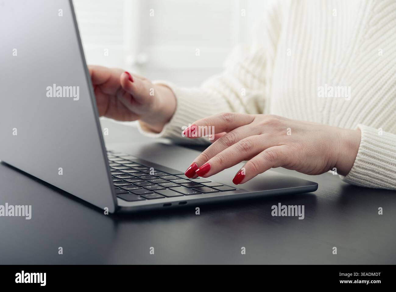 Close up of female hands with red manicure typing on a laptop keyboard. Concept of remote work, online communication, digital services, and modern lif Stock Photo