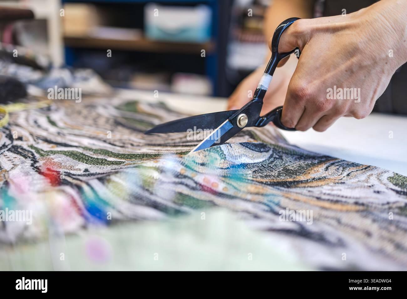 Cutting Fabric with Scissors on Worktable in Atelier Stock Photo