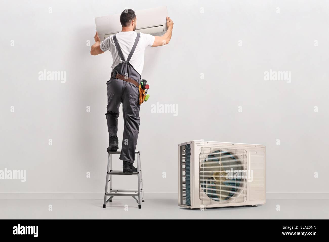 Technician on a ladder installing indoor air conditioning unit on a wall Stock Photo
