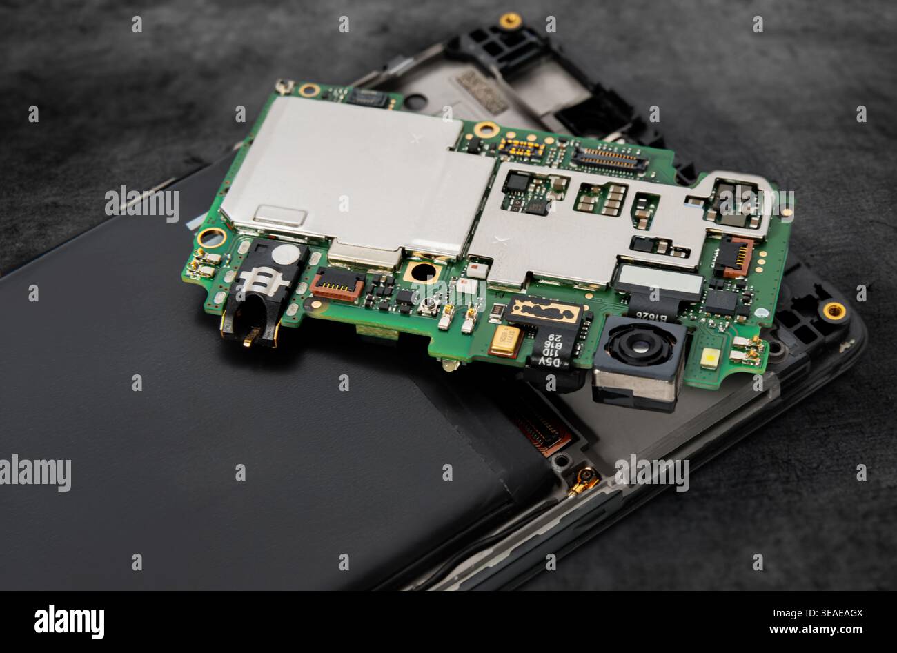 A technician is focused on repairing a smartphone that is disassembled on a work surface. Various parts are shown clearly. Stock Photo