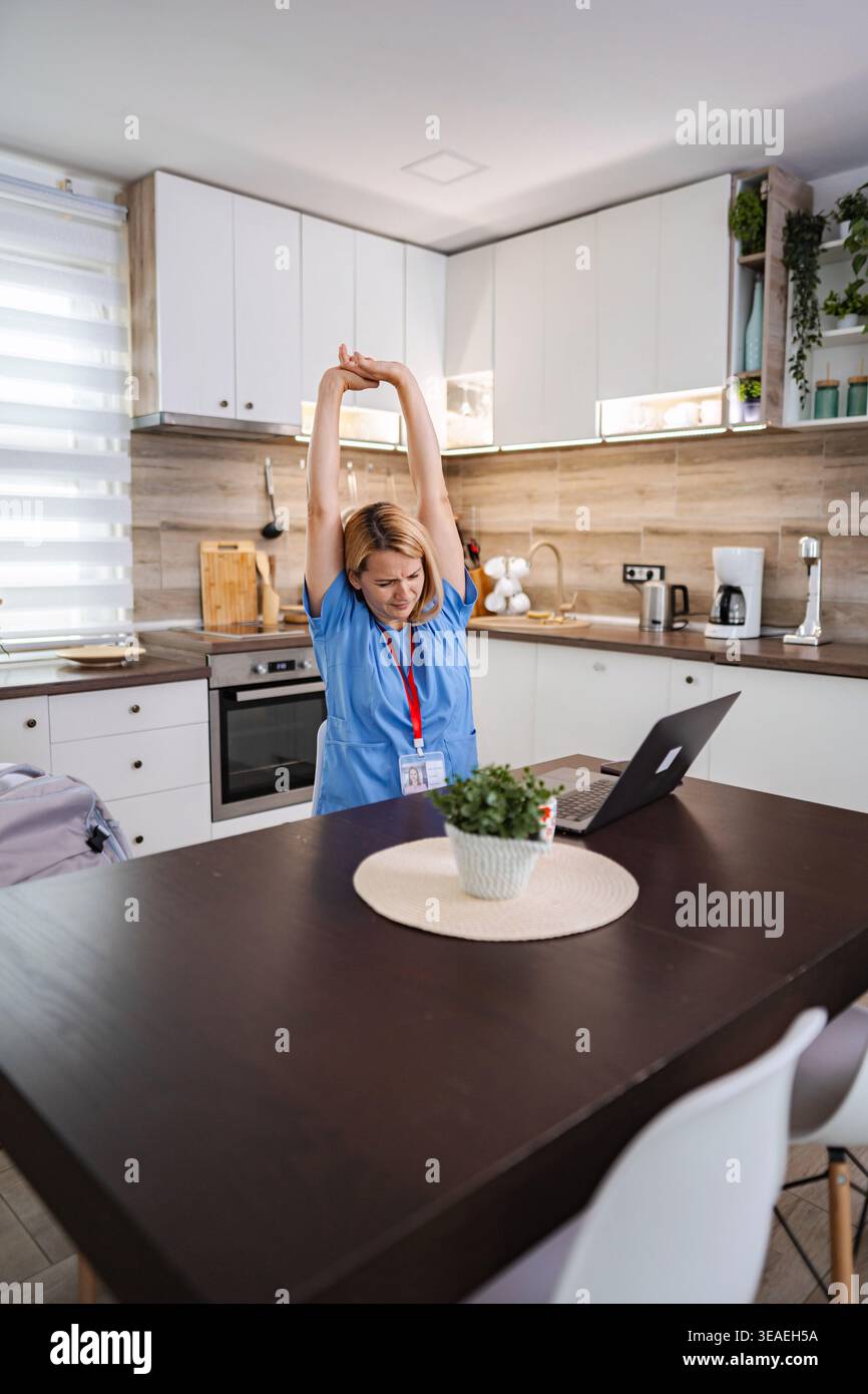 Female Doctor Stretching While Working From Home in Kitchen Stock Photo