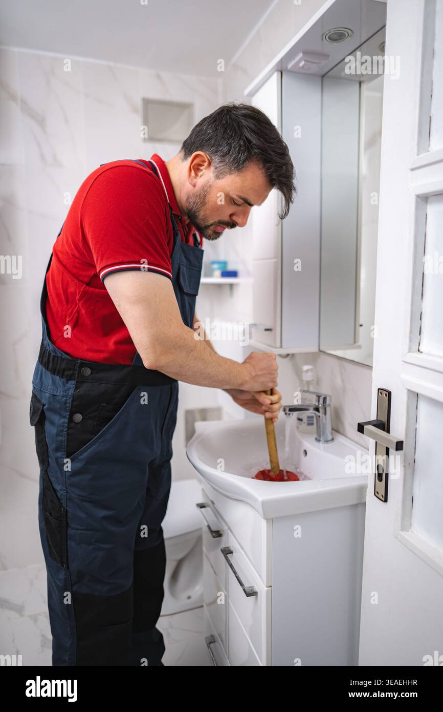 Plumber working using a plunger to unclog a bathroom sink Stock Photo