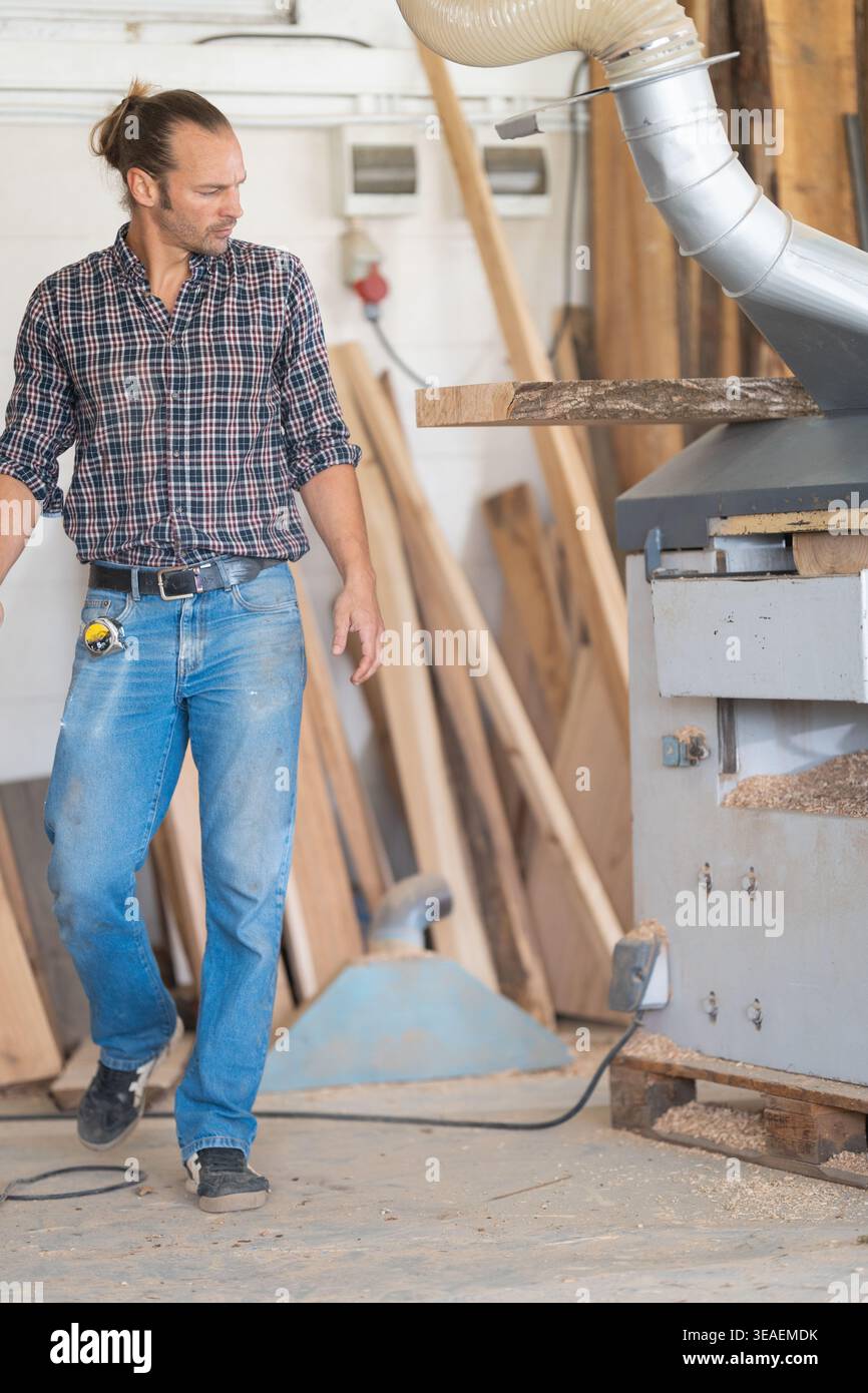 Woodworker operating planing machine in busy workshop Stock Photo