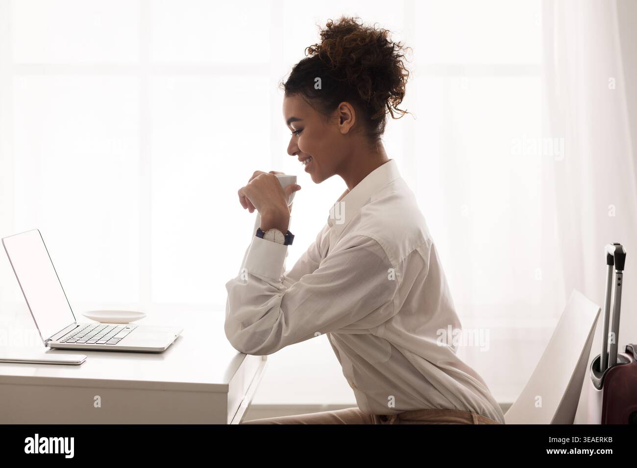 Young Woman Working Thoughtfully at a Desk With a Laptop in a Bright, Modern Room Stock Photo