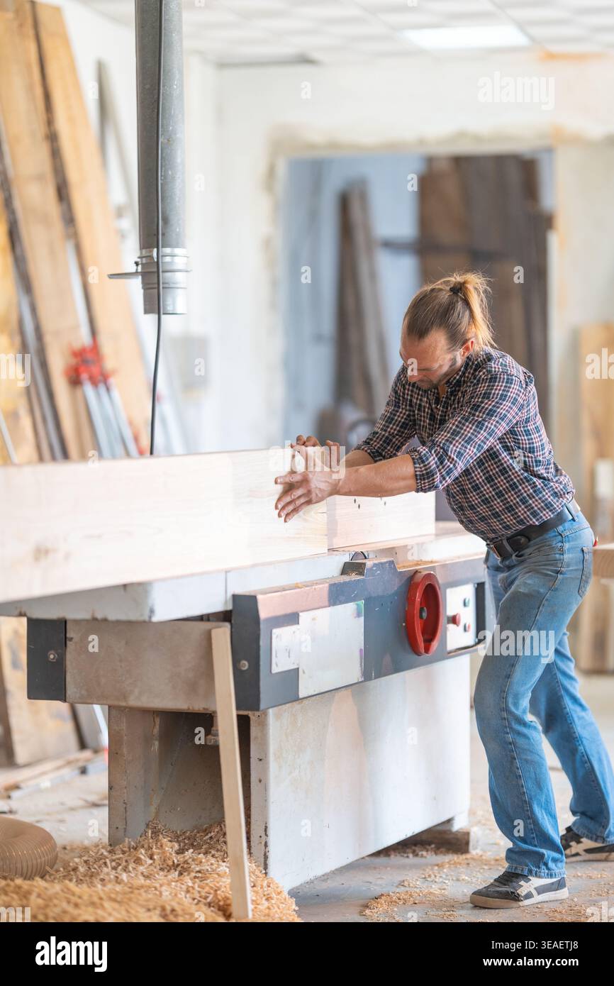 Woodworker flattening wood plank using jointer machine Stock Photo