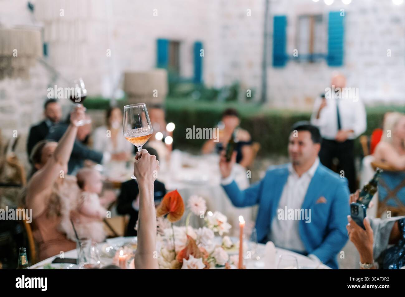 An energetic celebration where attendees raise glasses together amidst floral arrangements and shared laughter Stock Photo