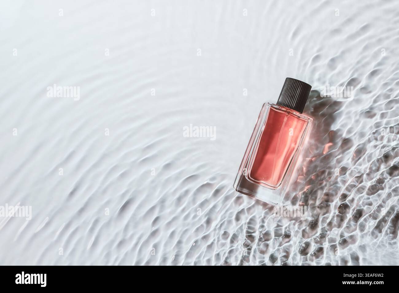 Perfume bottle laying on dynamic water surface creating elegant cool reflections Stock Photo