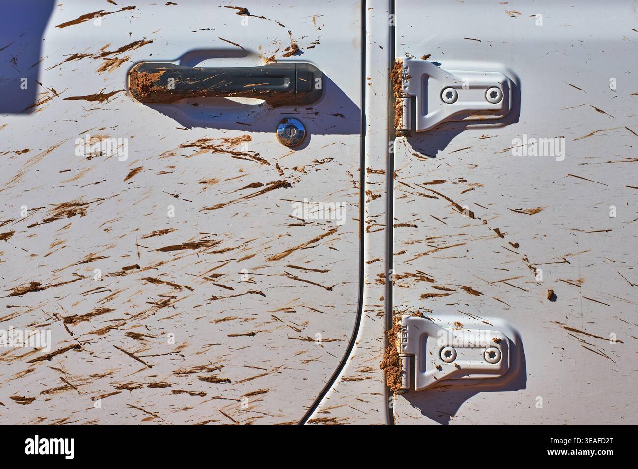 Muddy White Vehicle Door Close Up with Handle and Hinges in Harsh Sunlight Stock Photo