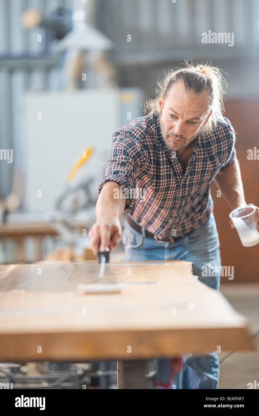 Carpenter applying protective epoxy resin to wood surface Stock Photo