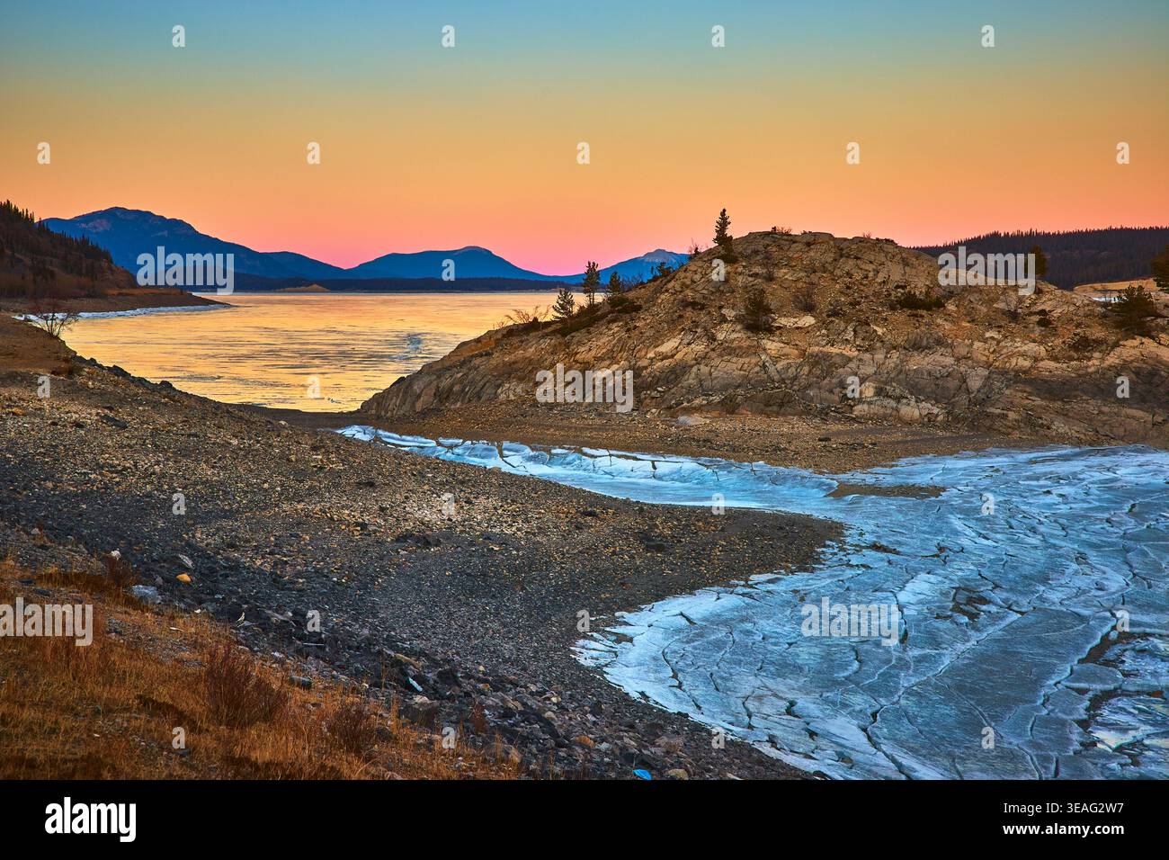 Frozen Lake Ice Cracks Rocky Shoreline and Sunset Sky in Winter Stock Photo
