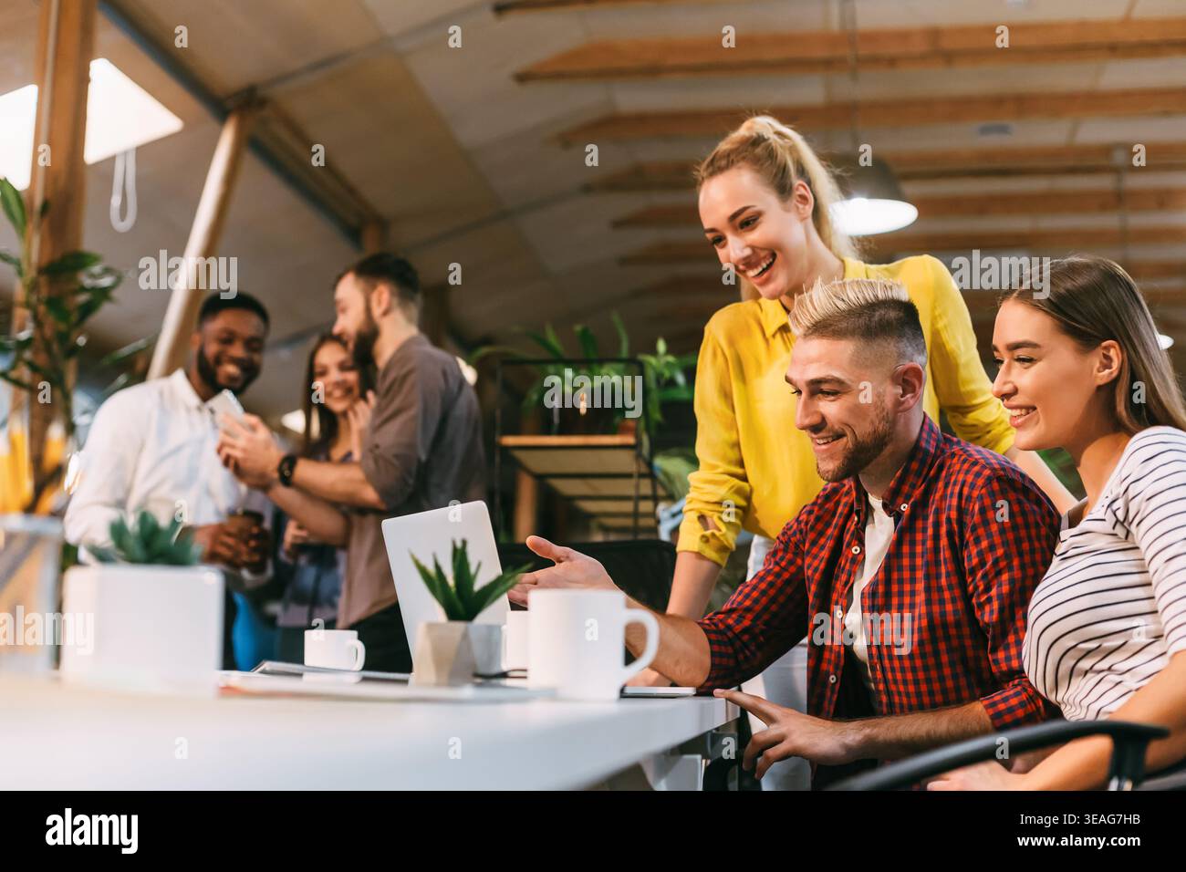 Young colleagues working on laptop and discussing new project Stock Photo