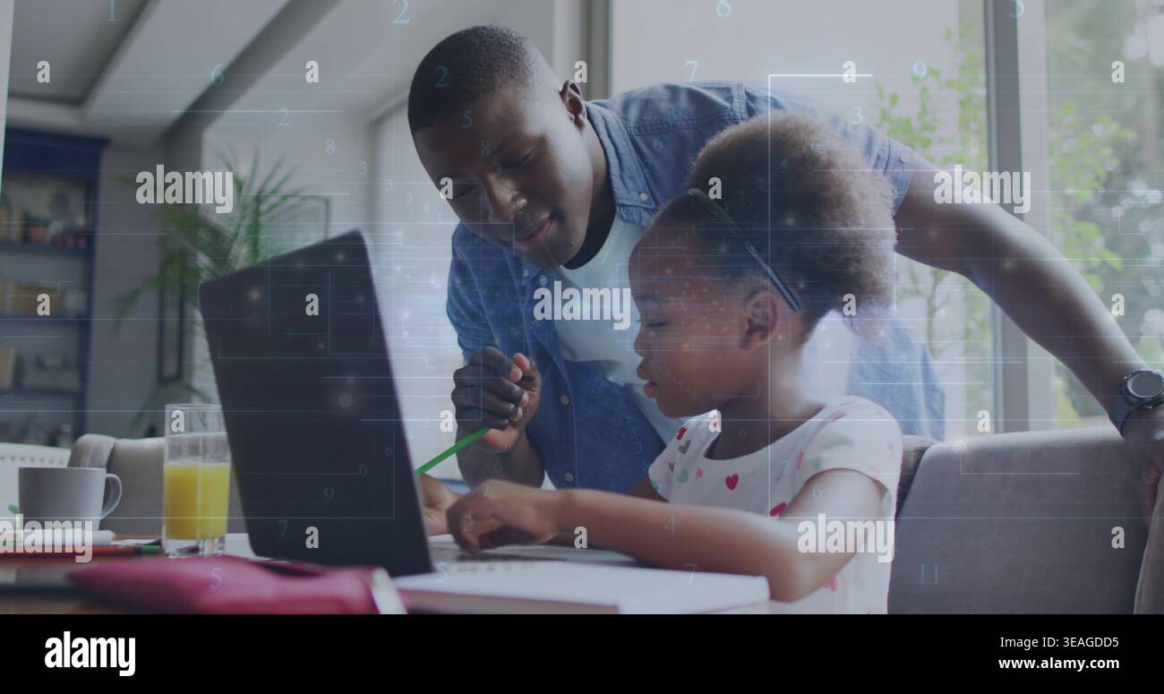 Guiding father in denim leaning over daughter using laptop at dining table holding green pencil Stock Photo