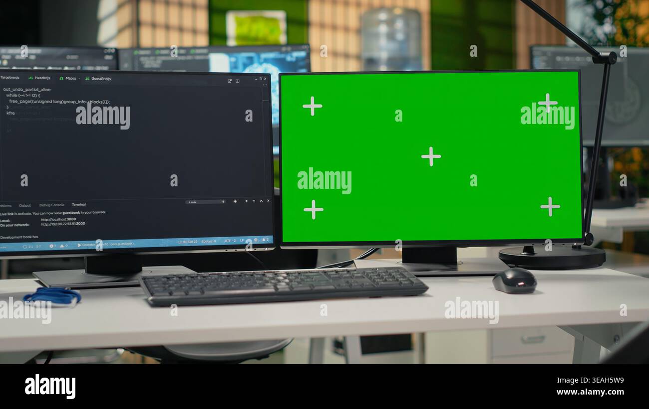Green screen PC in empty startup office with programming language script running on monitors. Mockup computers in AI industry startup workspace leveraging coding software enhancing system automation Stock Photo