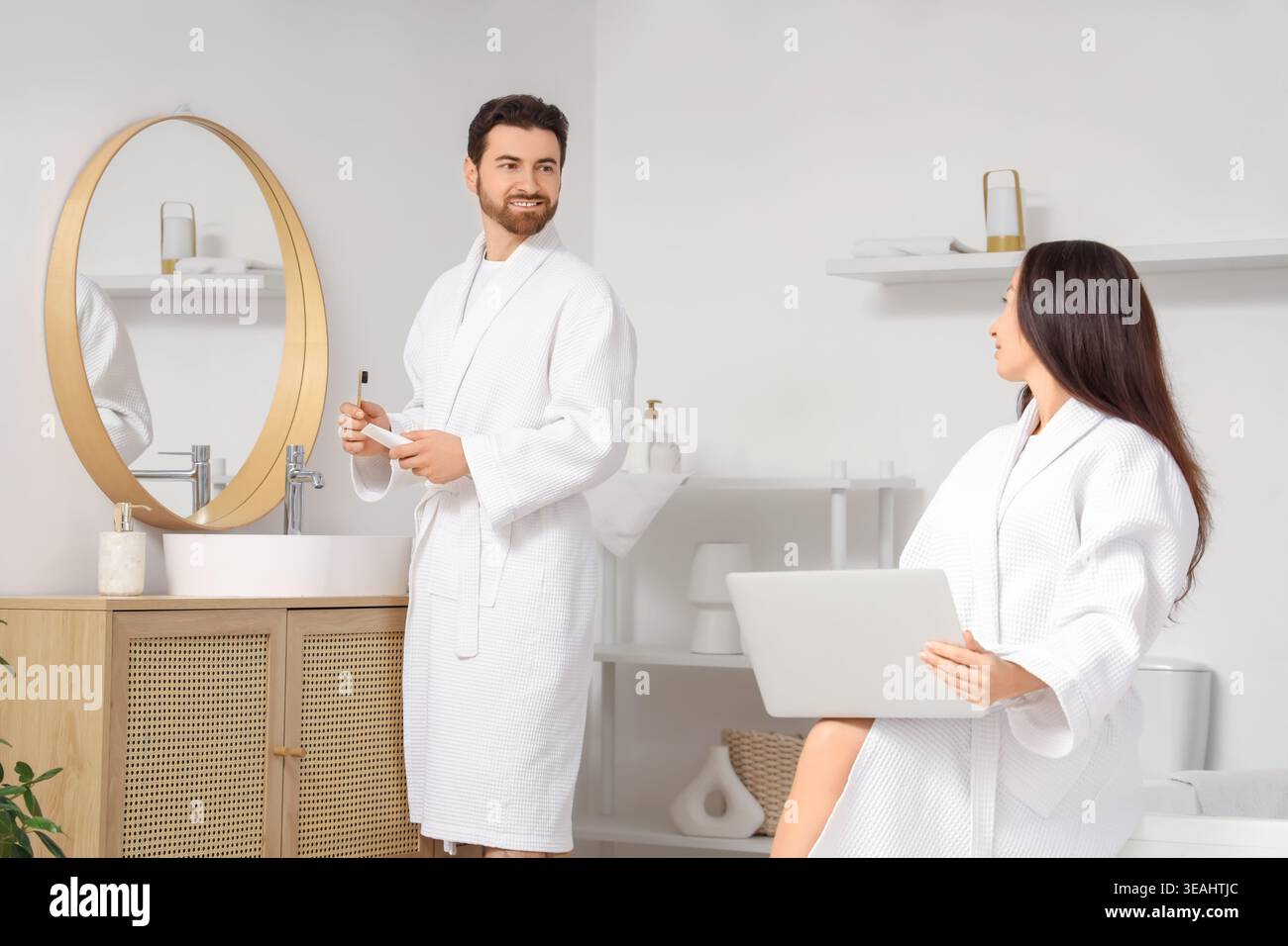 Handsome man brushing teeth while his wife using laptop in bathroom Stock Photo