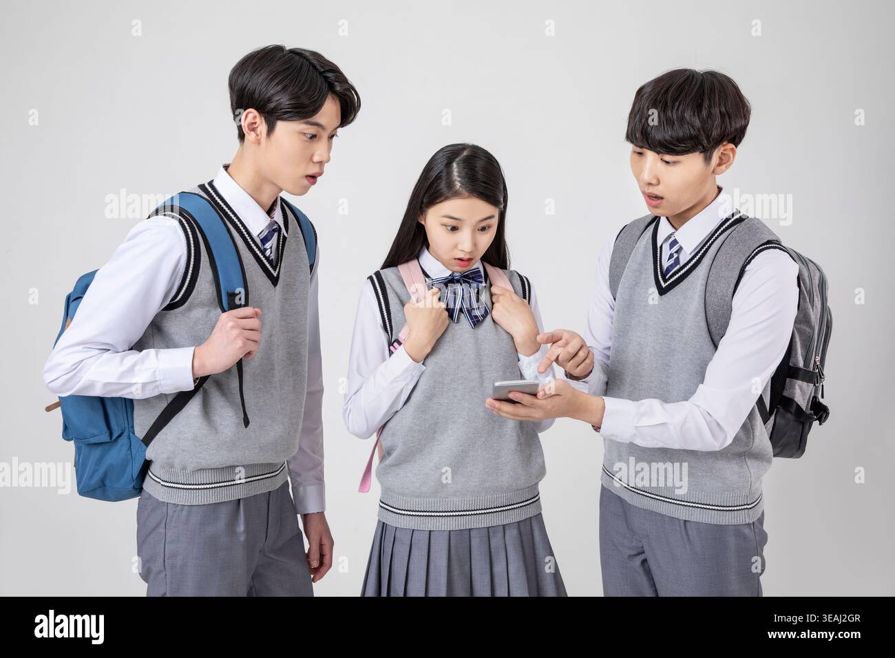 Three Asian teenagers in school uniforms look at a smartphone together ...
