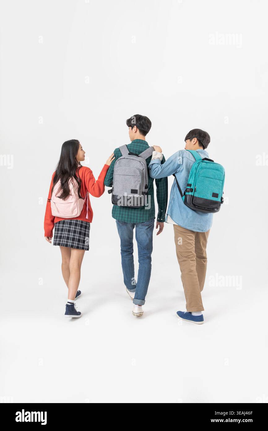 Three students walking together, wearing backpacks, against a white background. Stock Photo