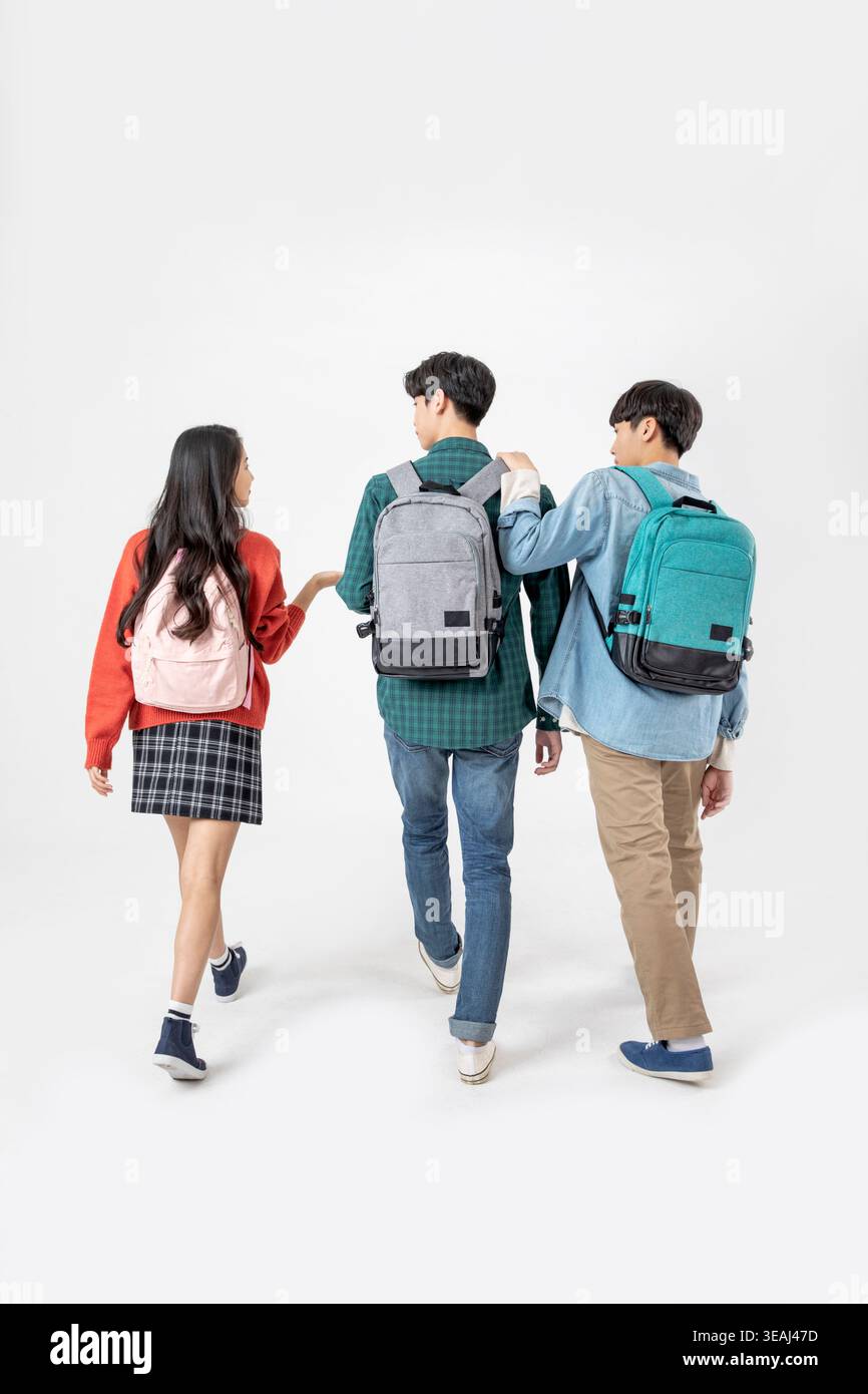 Three students walk together, wearing backpacks, in a neutral setting. Stock Photo