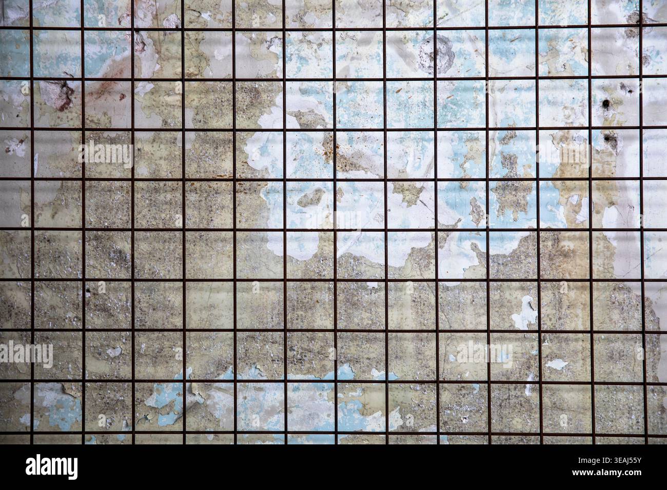 A weathered, rusty metal grid is exposed on a crumbling, ancient, stone wall. Stock Photo