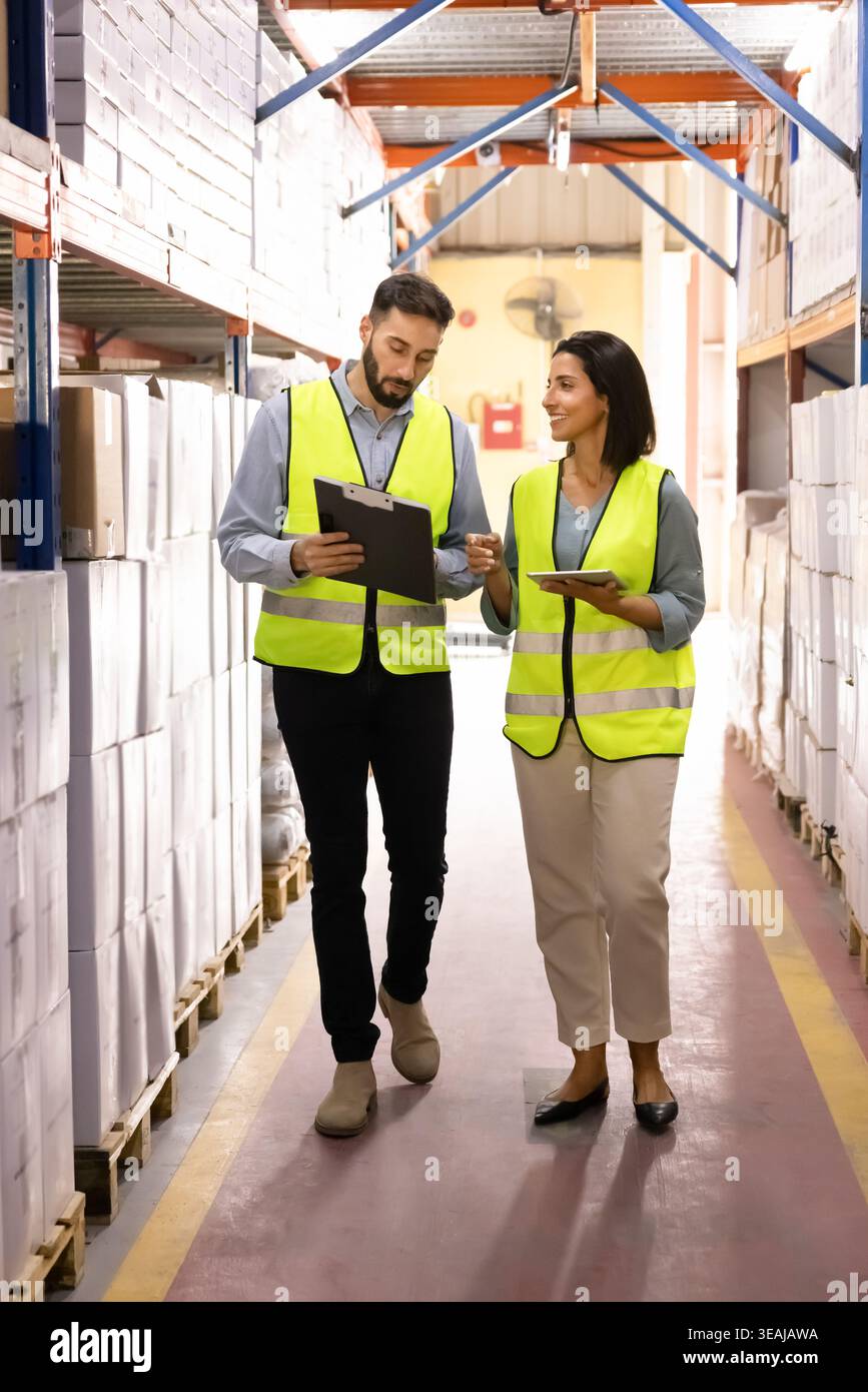 Warehouse workers talking, walking through stockroom aisle Stock Photo