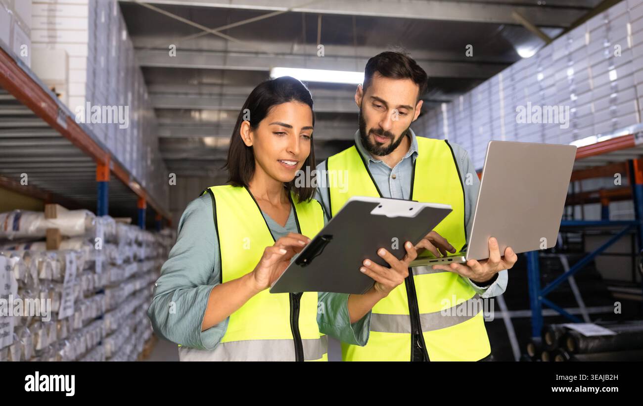 Two warehouse workers using laptop working together in storage aisle Stock Photo