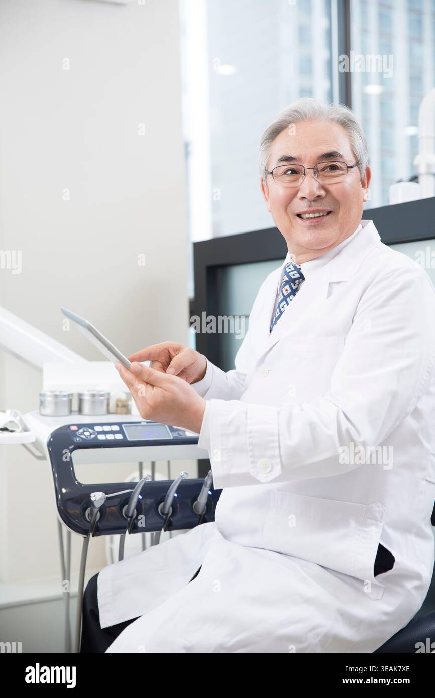 Smiling confident senior dentist using an electric tablet Stock Photo