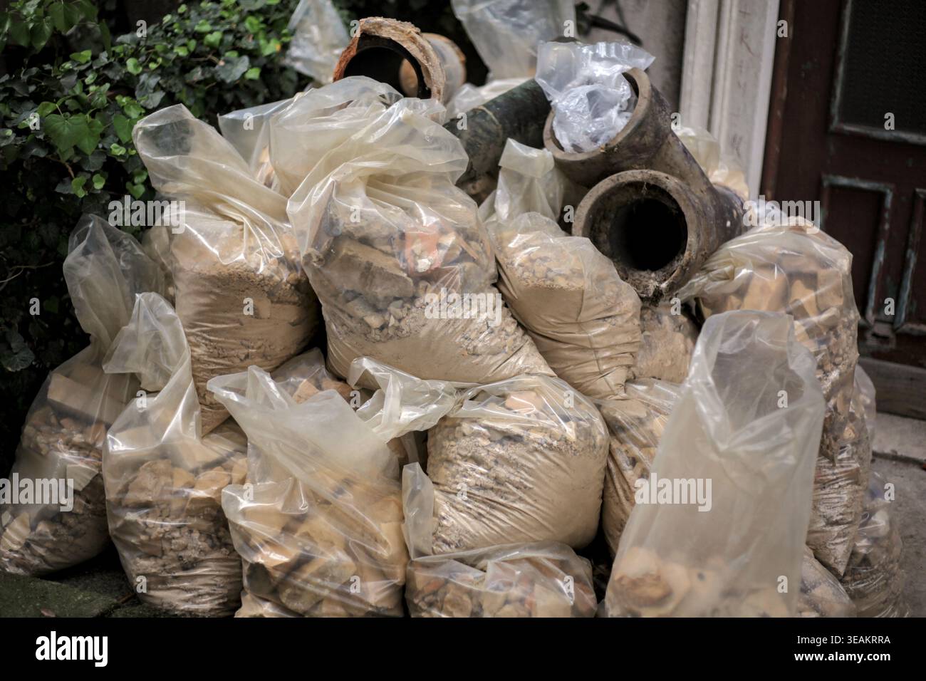 A pile of construction debris and rubble packed in plastic bags, with old pipes on top, ready for removal. Stock Photo