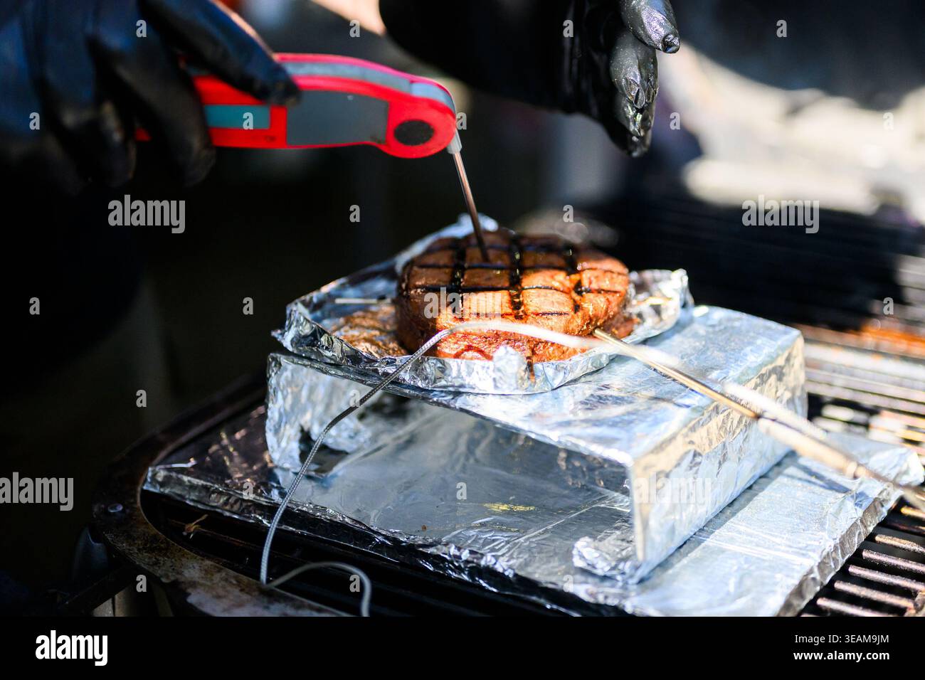A close-up action shot of a chef using a digital instant-read thermometer to check the internal temperature of a perfectly seared ribeye steak during Stock Photo
