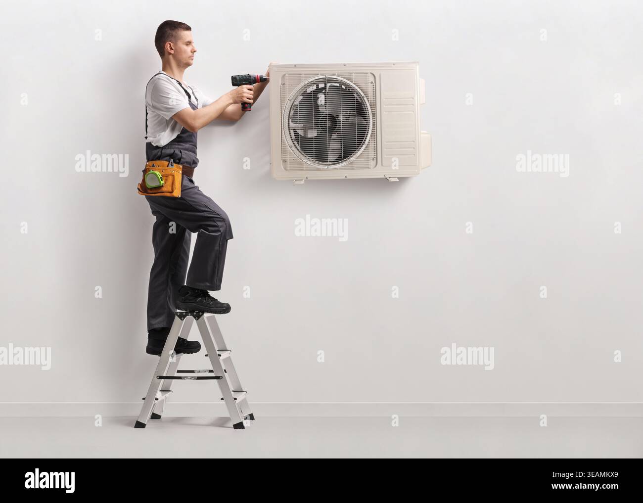 Technician installing an air conditioning unit on a wall with a drilling machine Stock Photo