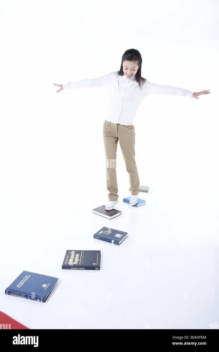 A young woman is balancing on a narrow path of books. Stock Photo