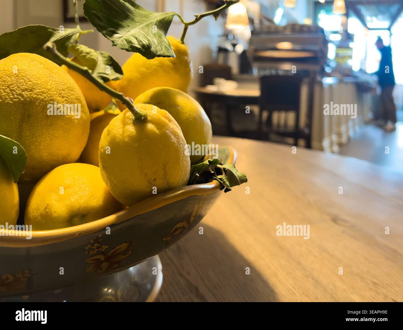 Citrus freshness on table, lemons in a bowl on wooden table inside cafe, creating bright natural accent and fresh food atmosphere, copy space Stock Photo