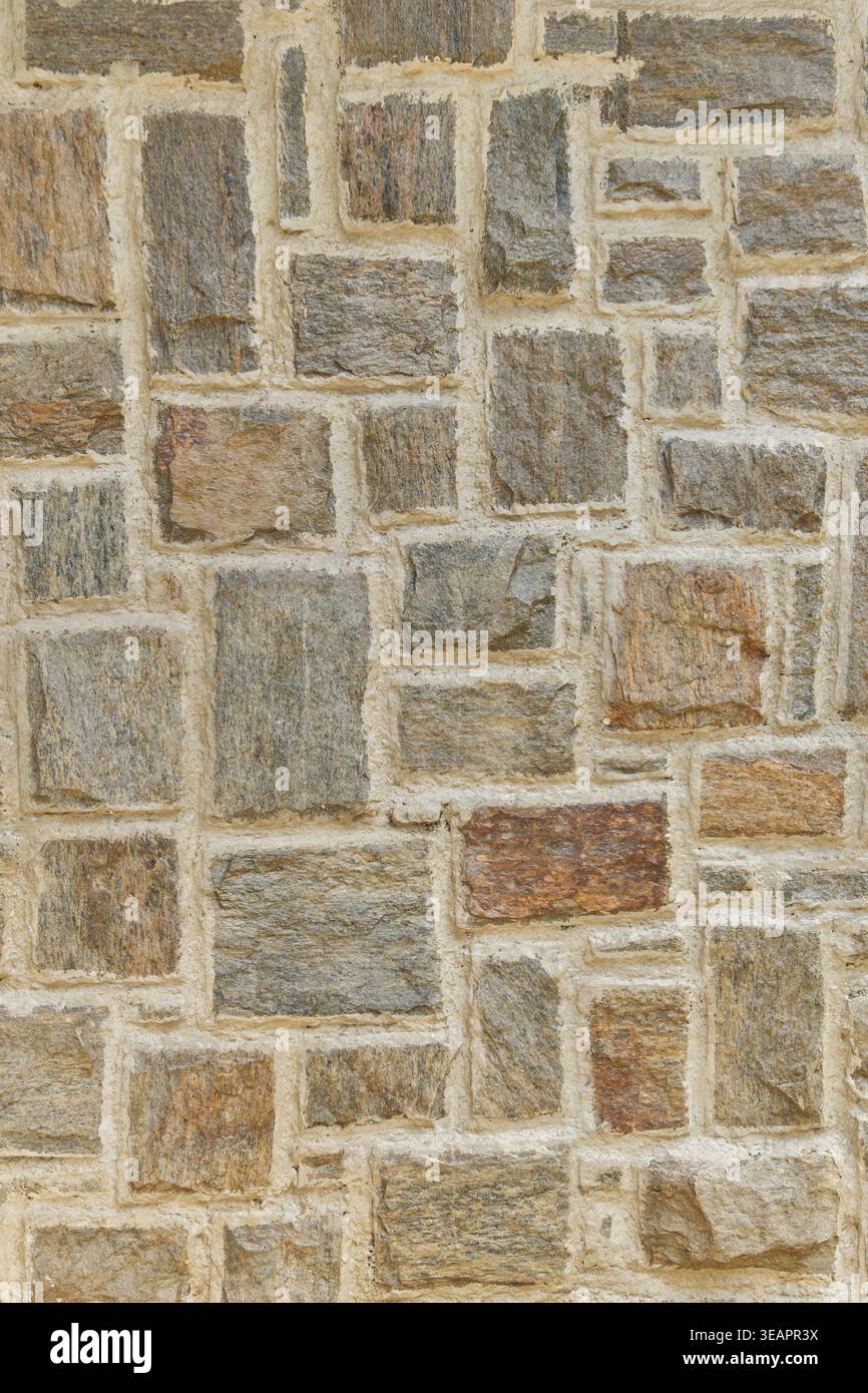 stone wall with rectangular grey and tan rocks in light mortar, vertical masonry surface with textured stone, full frame background, rustic building Stock Photo