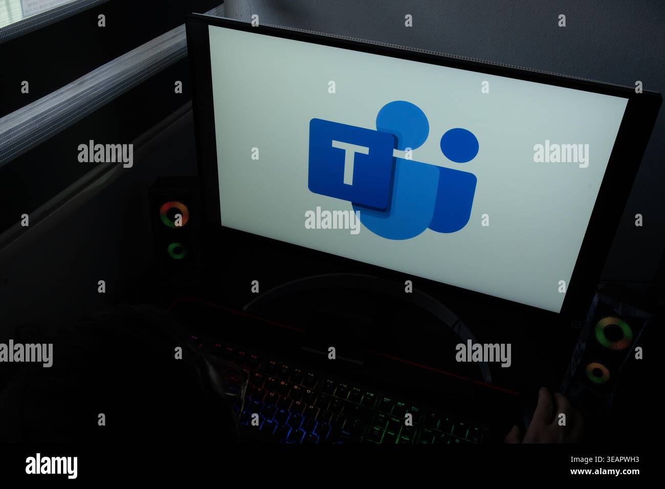 The Microsoft Teams communication platform logo is displayed on a computer monitor in a dark home office setting Stock Photo
