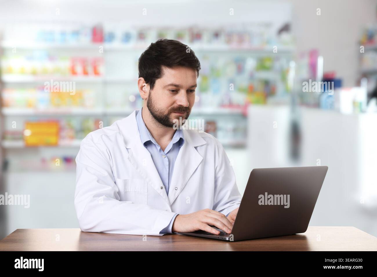 Pharmacist using laptop at table in drugstore Stock Photo