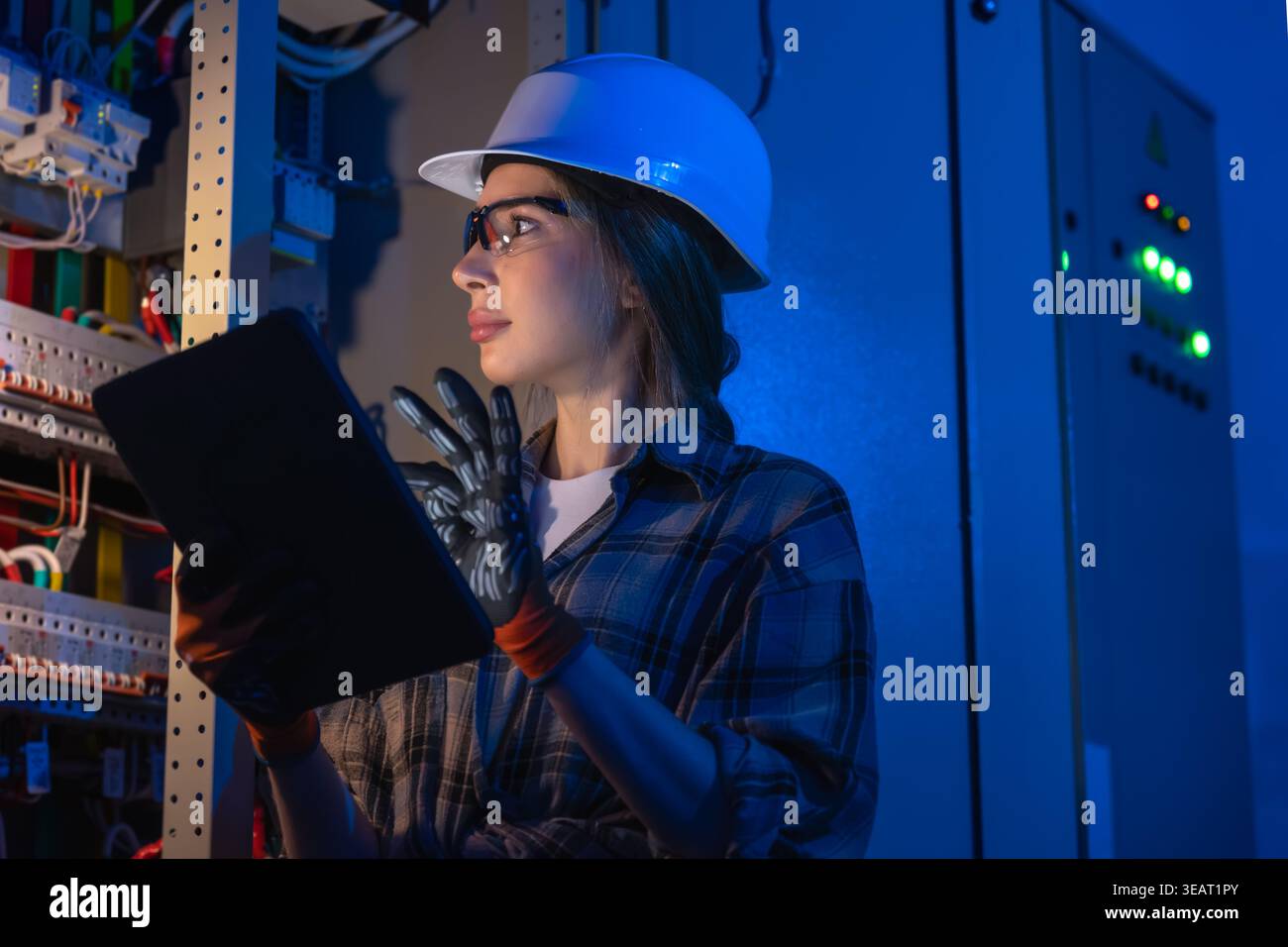 Female electrical engineer inspecting power system on tablet near switchboard. Digital control. Stock Photo