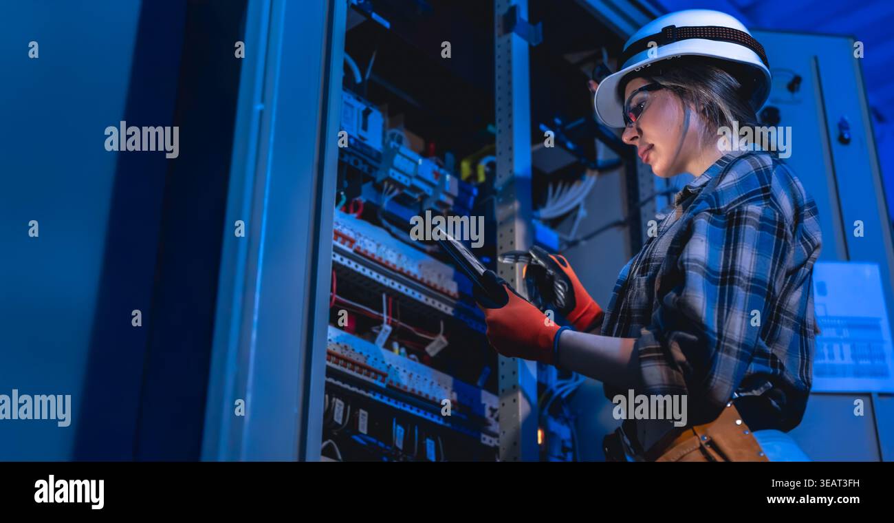 Female electrician inspecting electrical switchboard using tablet. Engineering service. Stock Photo