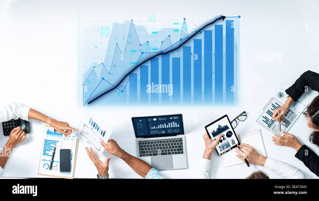 A diverse business team collaboratively engages in analyzing financial data, using technology and visual graphs within a modern office environment Stock Photo