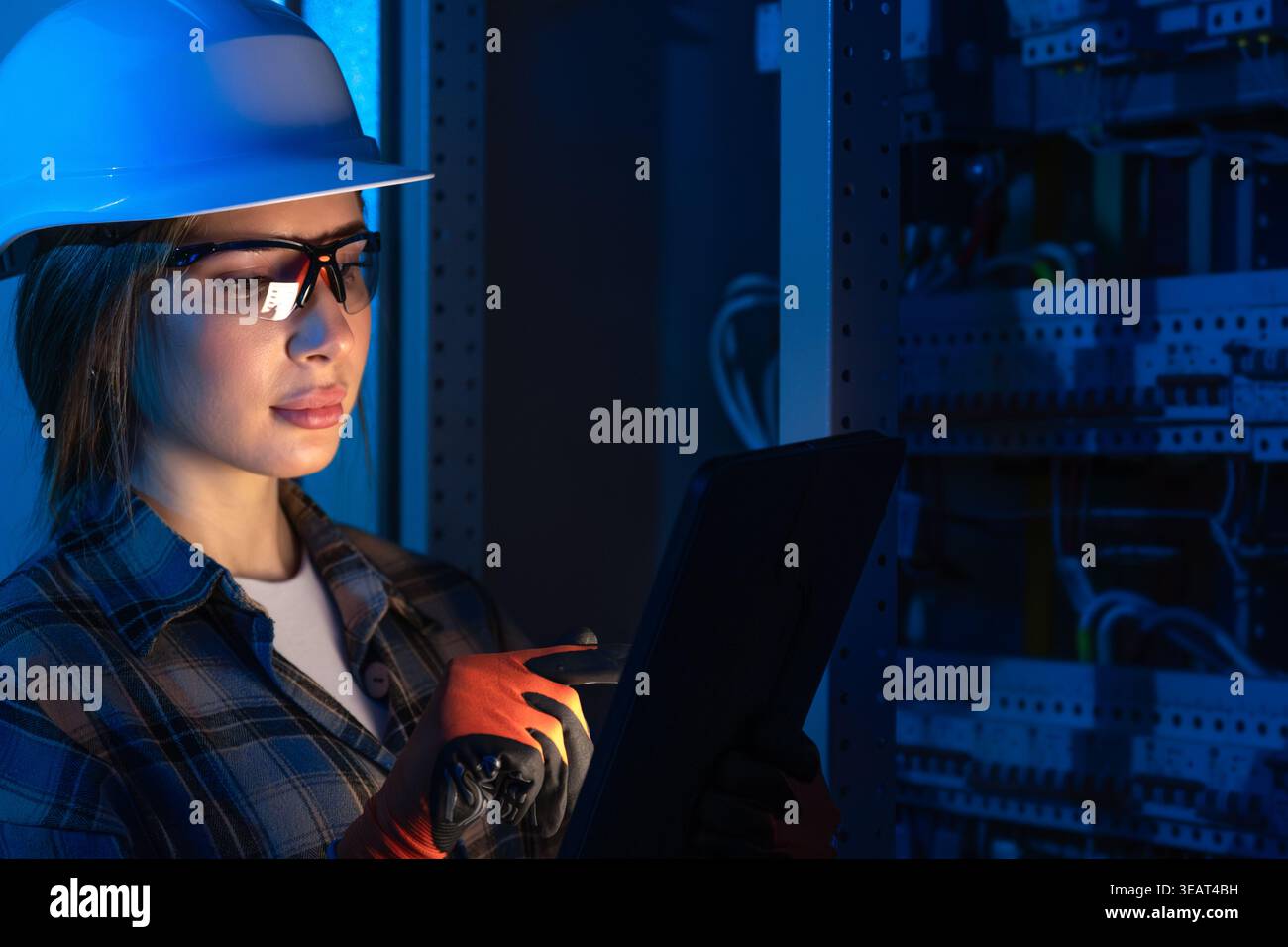 Electrical engineer analyzing power system using tablet near switchboard. Technical inspection. Stock Photo