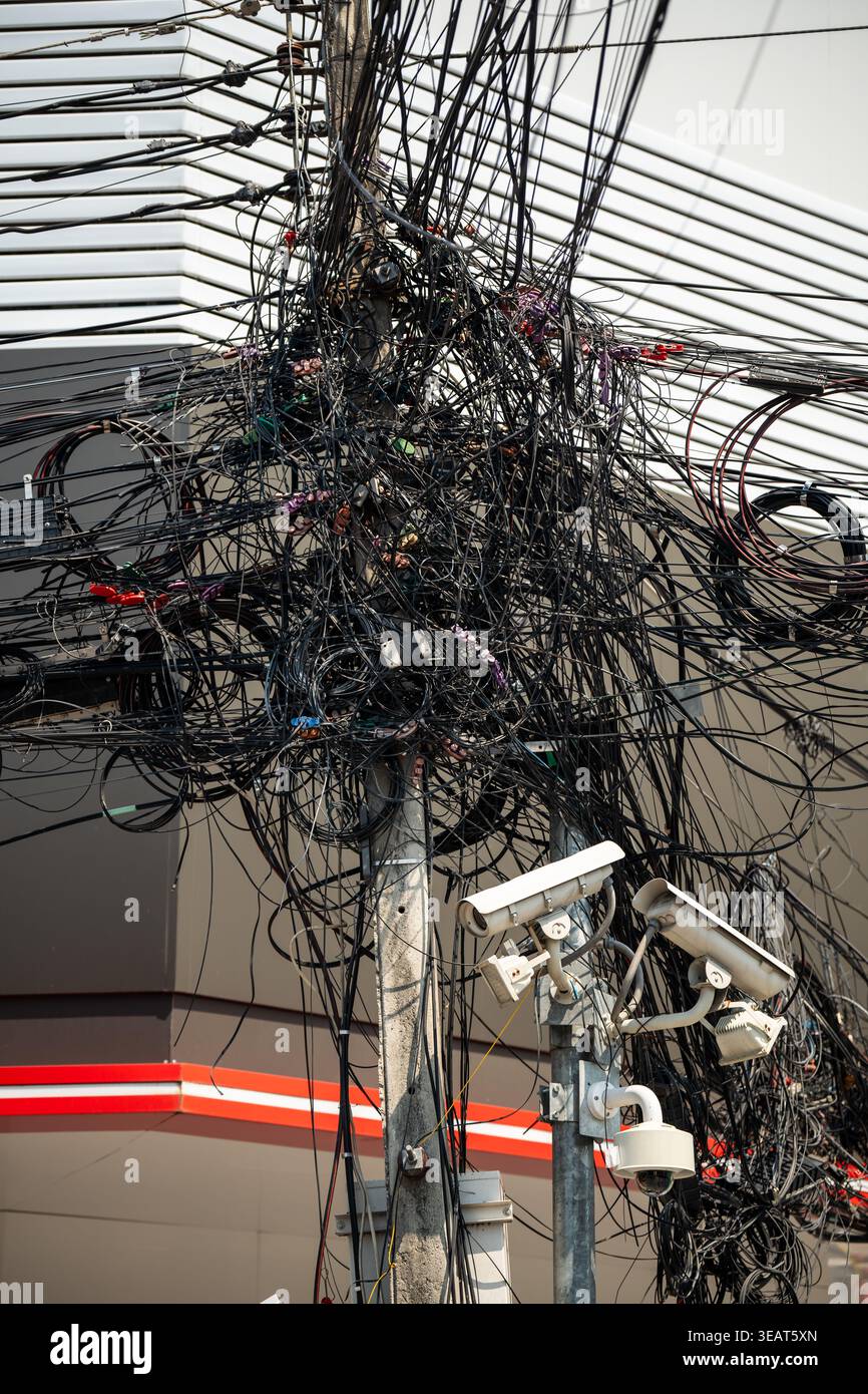 Messy tangled electricity wires and data cables on pole, asian urban landmark at street in city. Stock Photo