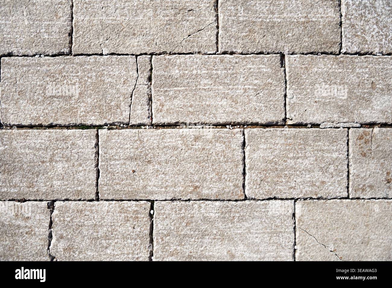 Weathered light gray stone wall texture with rectangular blocks and natural cracks. Ideal for architectural backgrounds or rustic design concepts Stock Photo