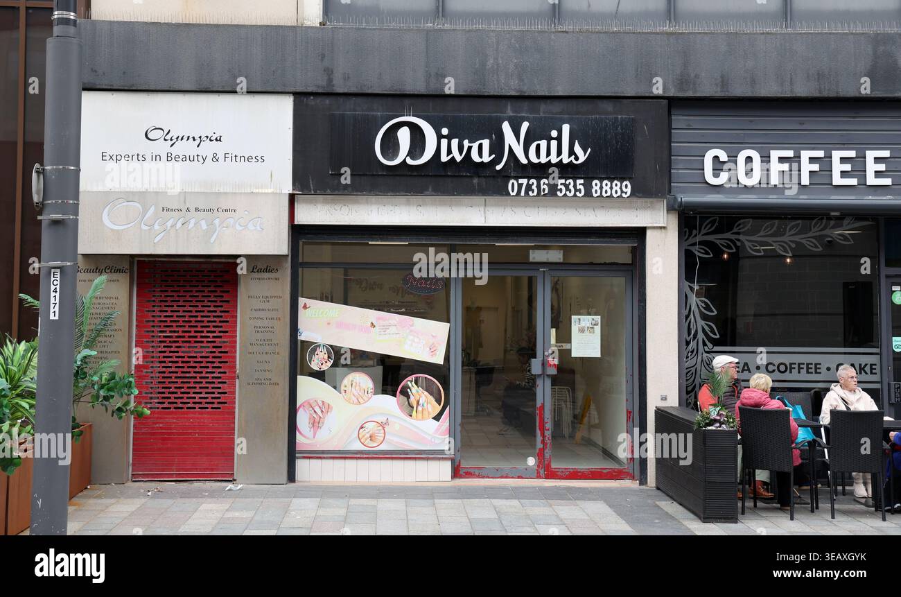 A nail salon called Diva Nails is seen on Sunderland High Street. The shop has a sign displaying its name and a contact number. Next to it is another establishment. People are seated outside at tables, enjoying their time. The scene reflects a typical day in the busy city center with foot traffic and local businesses contributing to the vibrant atmosphere. Stock Photo