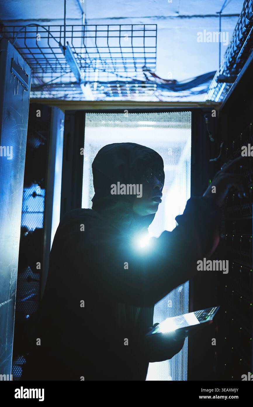 Person, hacker and tablet in data center at night for coding, cyber attack and ransomware. Suspicious, criminal and digital with code script for Stock Photo