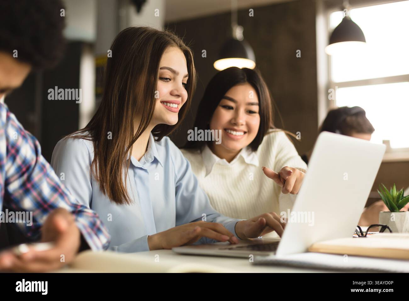 Two Friends Collaborate on a Laptop in a Modern Workspace While Smiling and Discussing Ideas Stock Photo