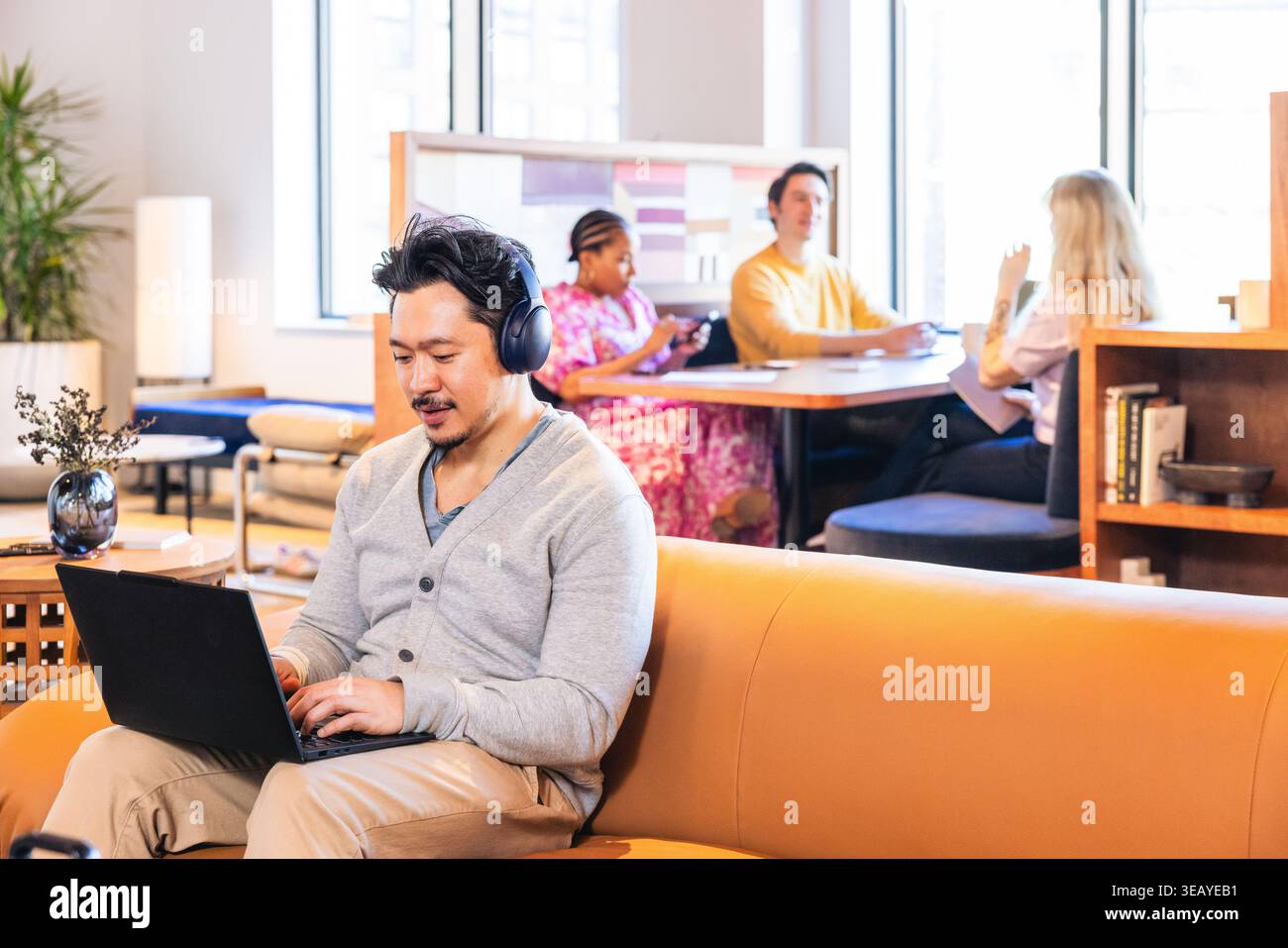 Asian Businessman Smiling and using headphones while on computer Stock Photo