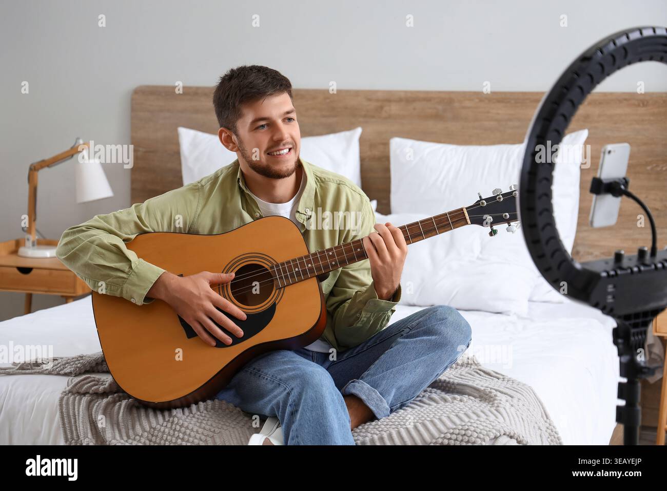Young bearded man playing guitar while recording video in bedroom Stock Photo
