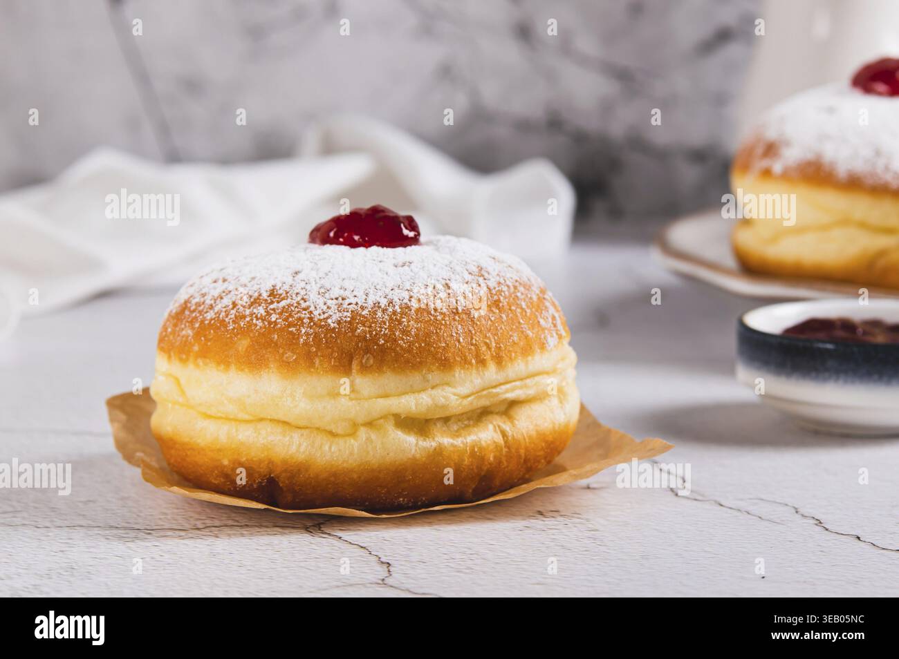 Delicious jam donuts in powdered sugar on parchment paper on the table Stock Photo